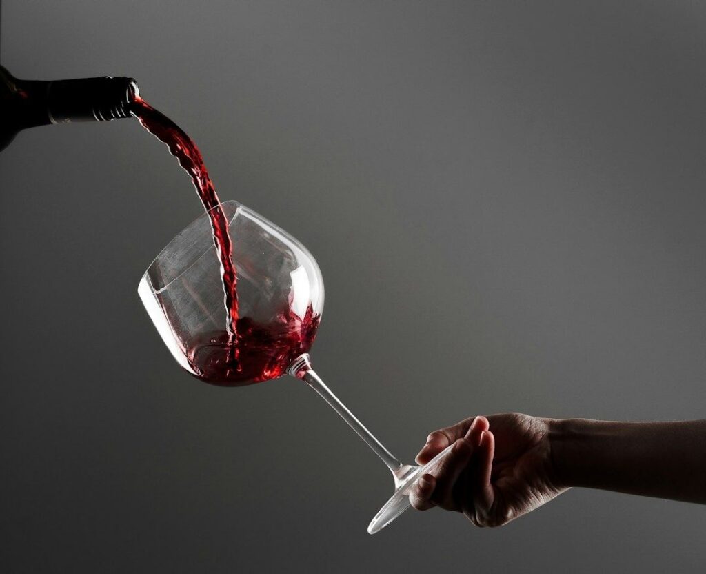 Red wine being poured into a tilted glass held by hand