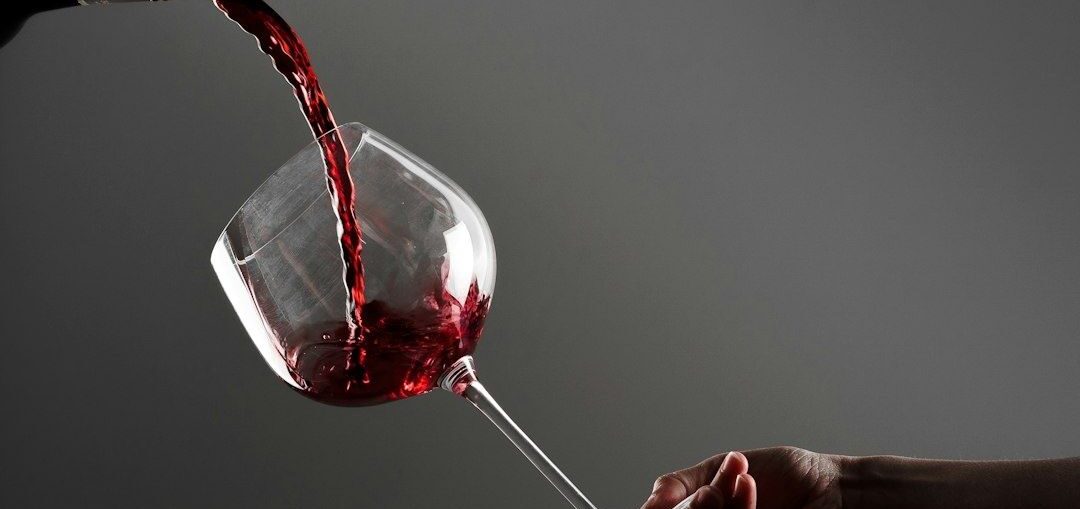 Red wine being poured into a tilted glass held by hand